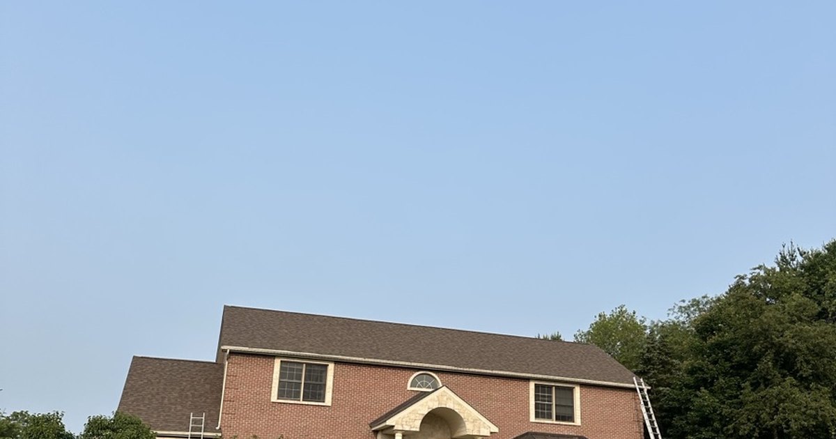 Brick two-story house with a brown shingle roof and ladders at both ends