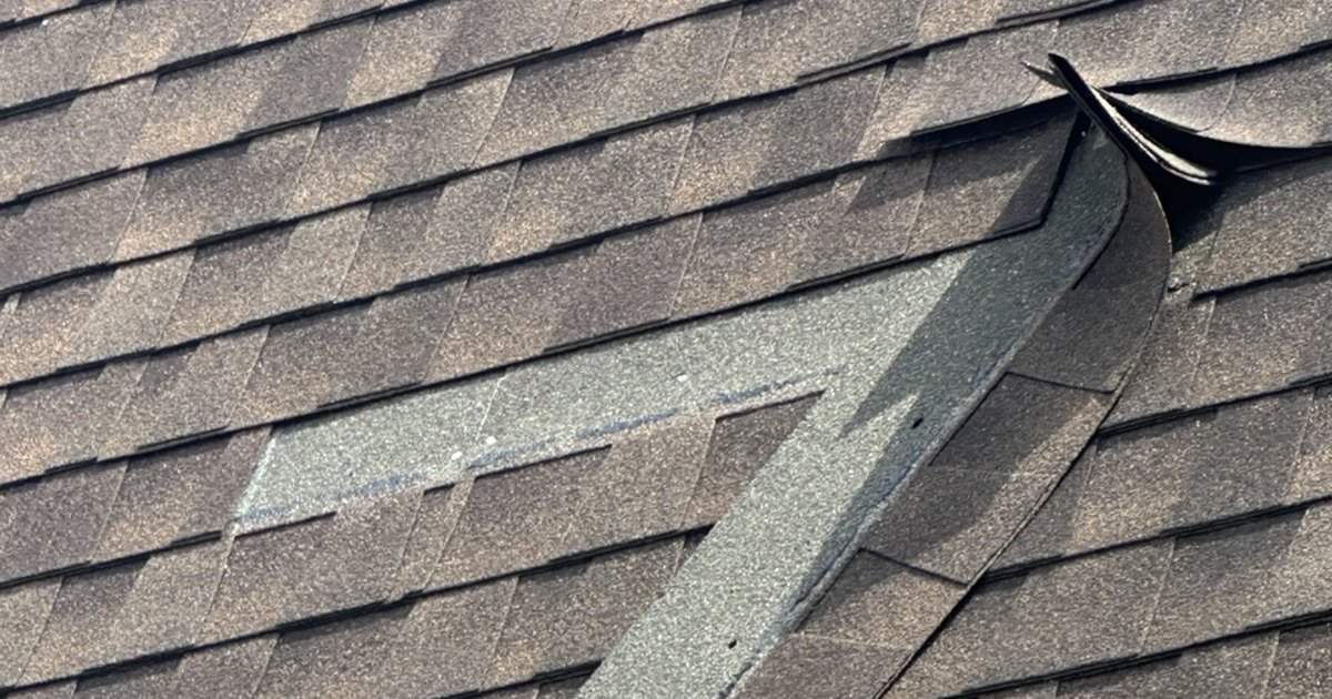 Torn asphalt shingle peeled back on a roof slope, exposing the course underneath