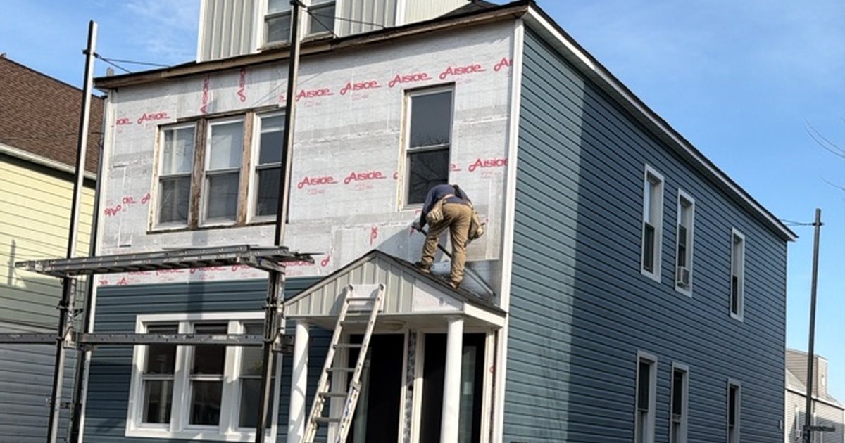 Crew installing blue siding over new house wrap on a two-and-a-half-story house