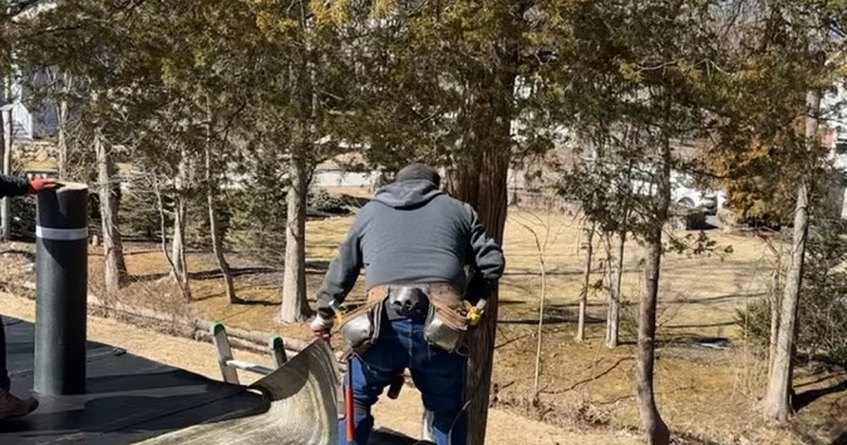 Roofer working on a flat roof membrane beside a pipe stack, with trees behind the house