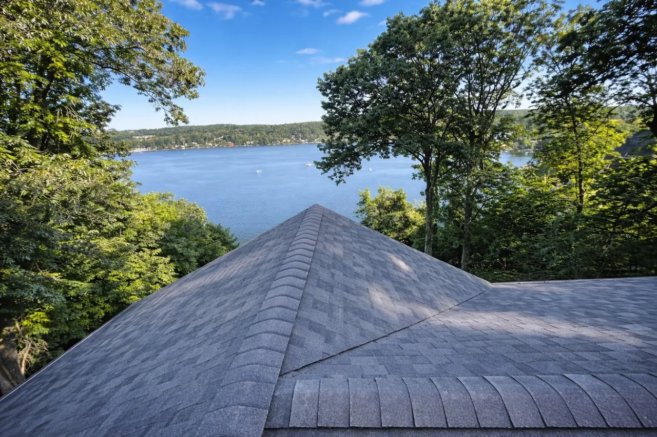 Gray asphalt shingle hip roof with trees and a lake beyond it
