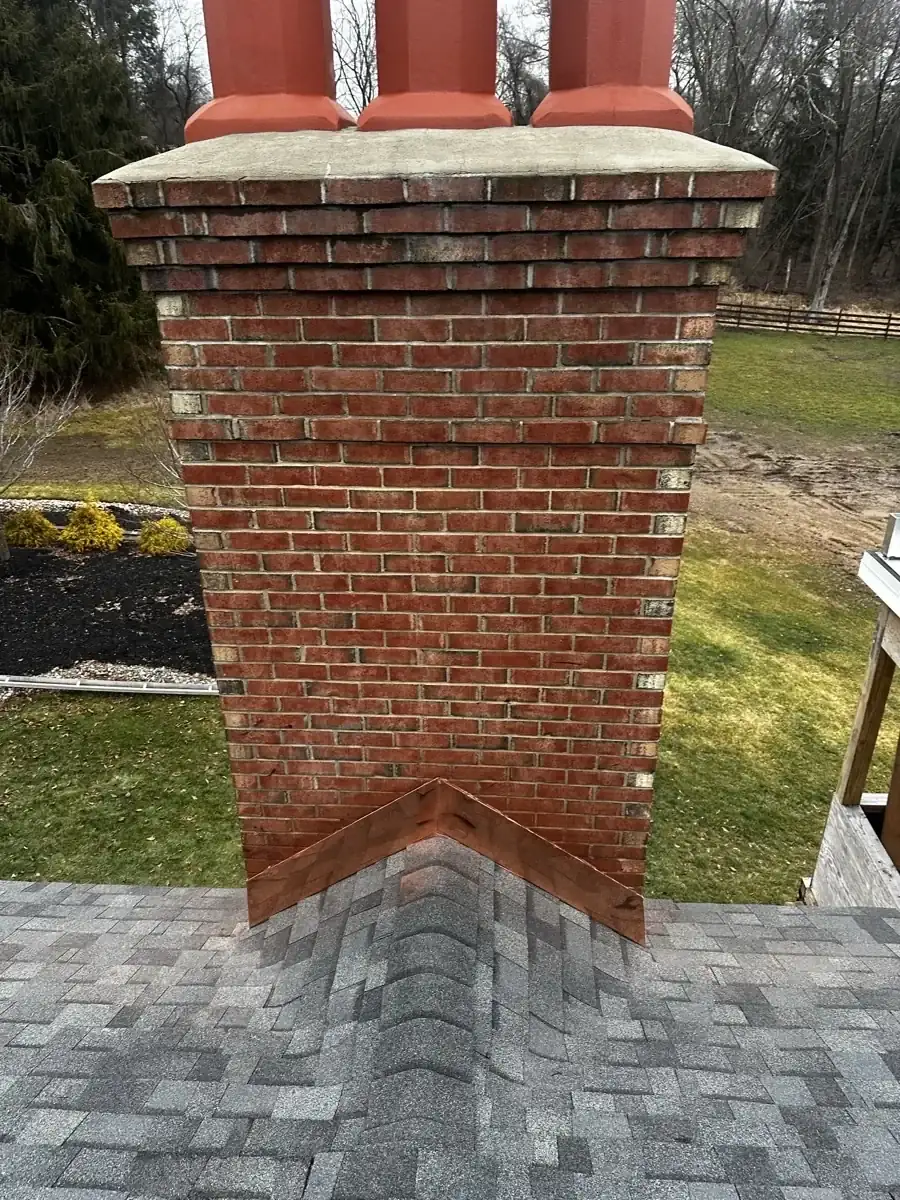 Brick chimney with metal flashing above gray roof shingles